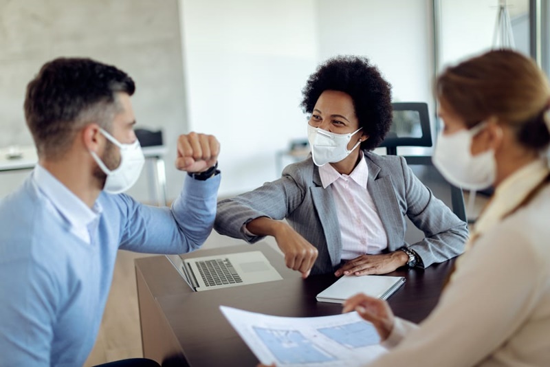 Pessoas usando máscaras se cumprimentam com os cotovelos durante uma reunião.